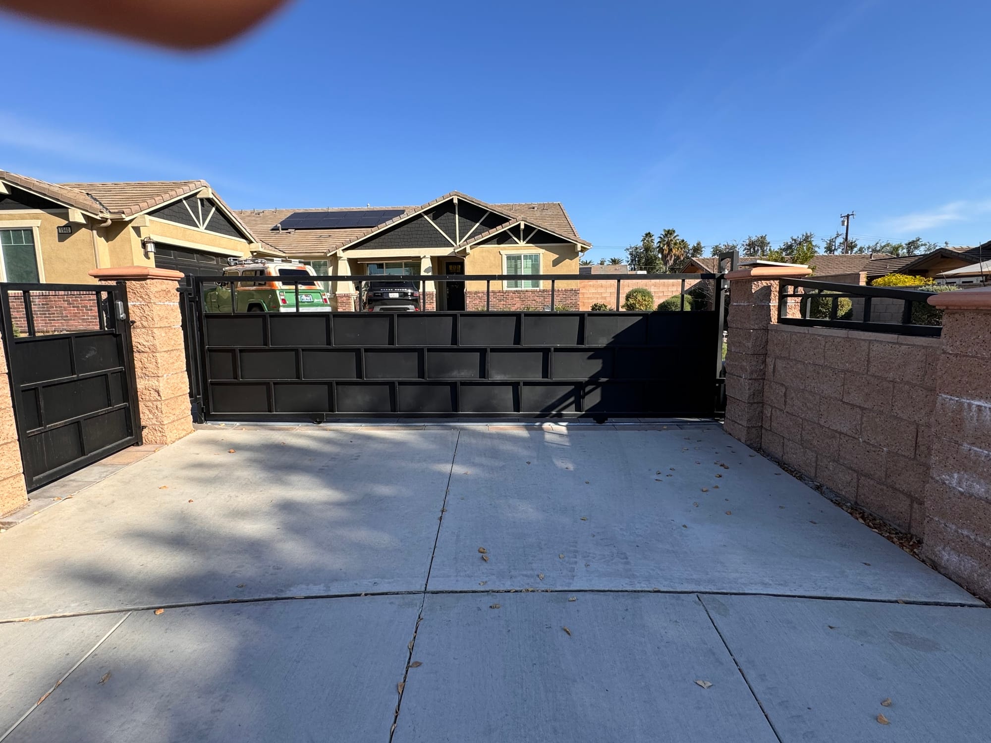 A black metal sliding driveway gate across a residential driveway in Menifee, California